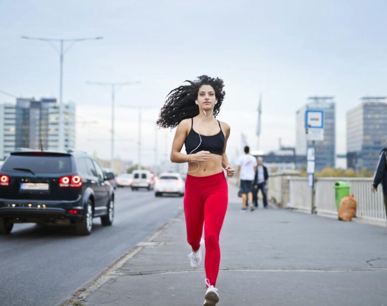 A fit woman with curly hair runs on a city street, enjoying music and staying healthy.