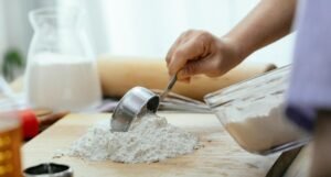 A woman measuring flour with a scoop during baking in a home kitchen.