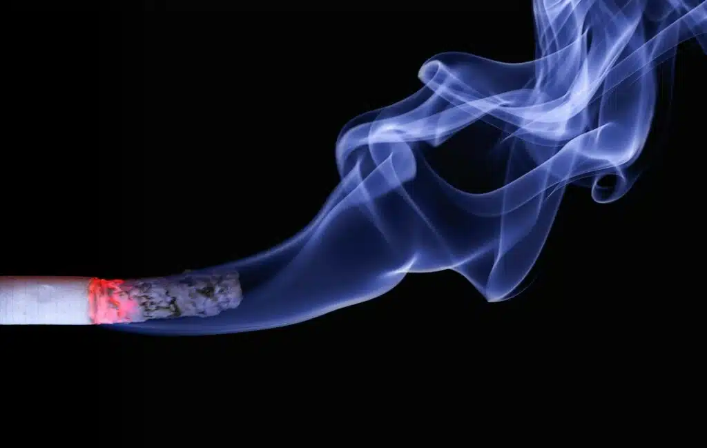 Detailed close-up of a cigarette with glowing ember and swirling smoke on a black background.